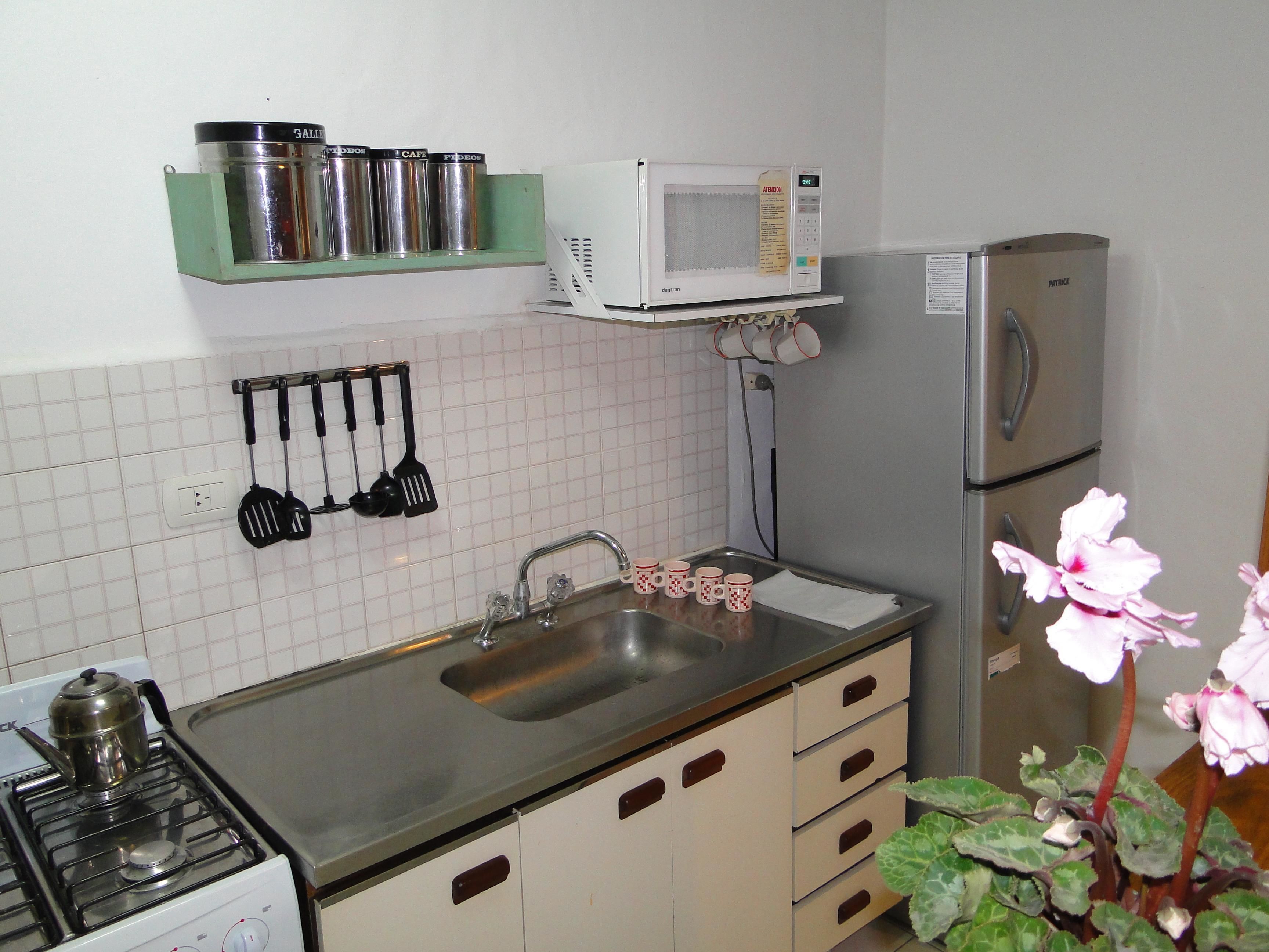 Una cocina equipada con estufa, lavaplatos, microondas, refrigerador y utensilios colgantes.