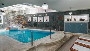 An indoor swimming pool with stone walls, a glass ceiling, and a tiled floor.