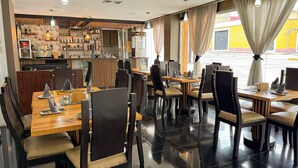 A restaurant with a bar area, multiple dining tables with chairs, and a view of the street outside. - Hotel Tibisay  (Milla)