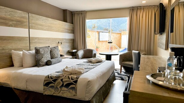 A hotel room with a large bed, a desk with a coffee maker, a chair, and a view of the outdoors. - Hotel Tibisay  (Milla)