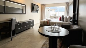 A modern living room with a flat-screen TV, a dining table, a sofa, and a large window offering a view of the outdoors. - Hotel Tibisay  (Milla)