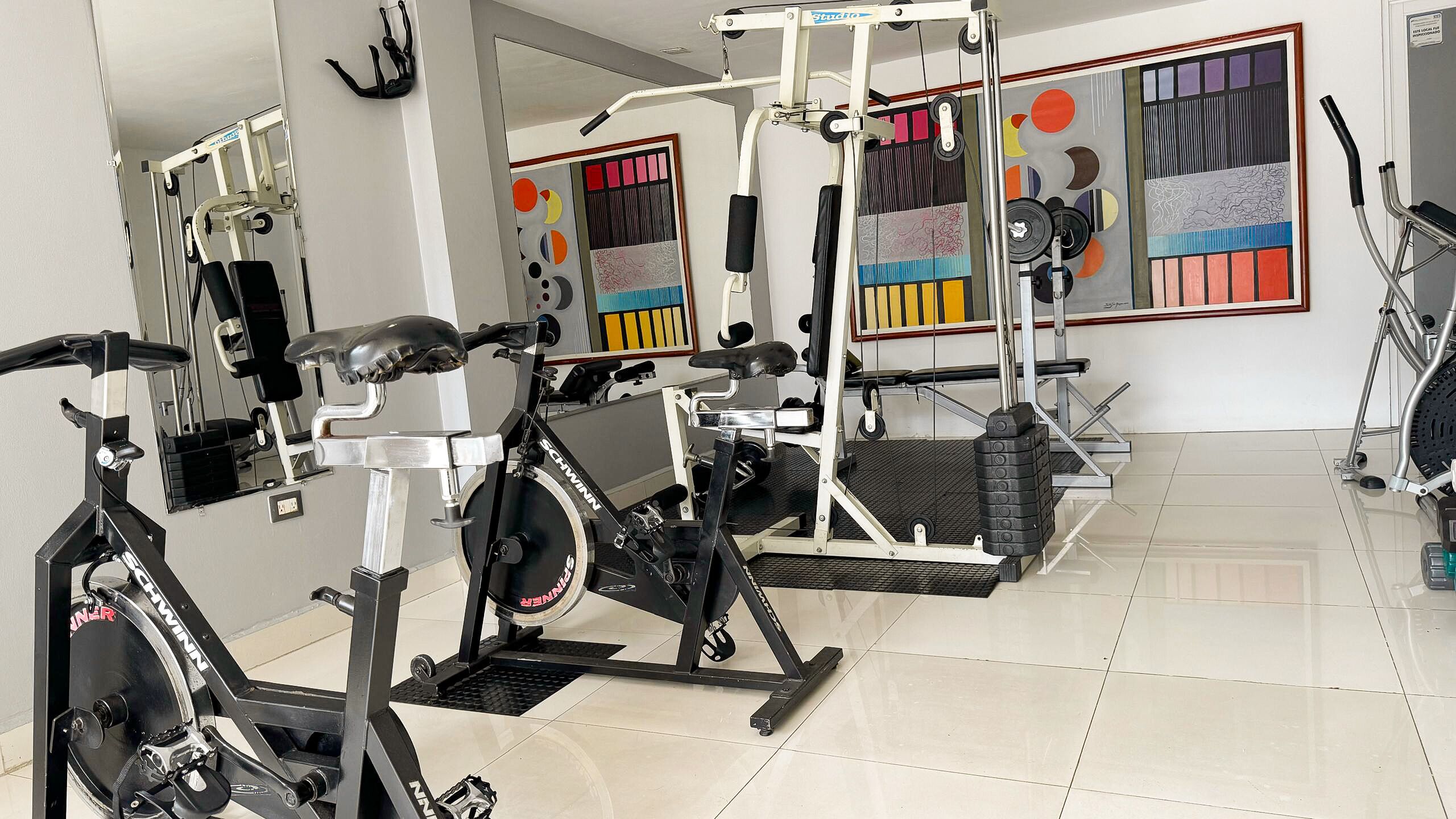 A gym with stationary bikes, weight machines, and a mirrored wall.
