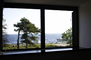 A room with a large window overlooking a beach with trees and a pier. - Smygehus Havsbad (Trelleborg)