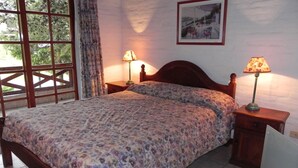 Un dormitorio con cama de madera, cubrecama floral, dos lámparas de noche, una ventana con cortinas y un cuadro en la pared.