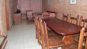 Un comedor con una larga mesa de madera y sillas, un mueble pequeño y una cortina.