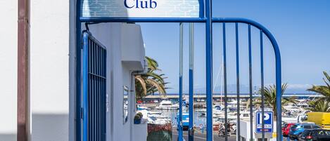 L'ingresso di un edificio con un cartello che riporta 'Apartamentos Puerto Colon Club' e vista su un porto turistico con barche.