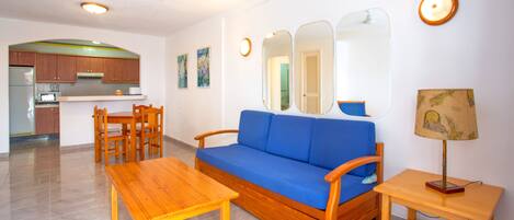 Un salon avec un canapé bleu, une table basse en bois et une petite table d’appoint avec une lampe.