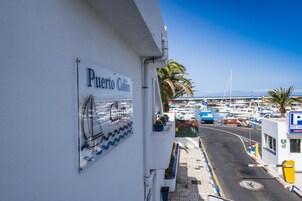 Vista de la calle con un cartel de Puerto Colón, una marina con barcos y un cartel de estacionamiento.