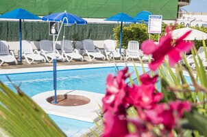 Un área de piscina con sillones blancos y sombrillas azules.