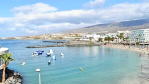 Zona costera con playa, barcos y un faro.