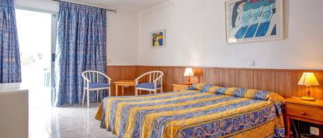 A hotel room with a bed, two chairs, a table, and a lamp.