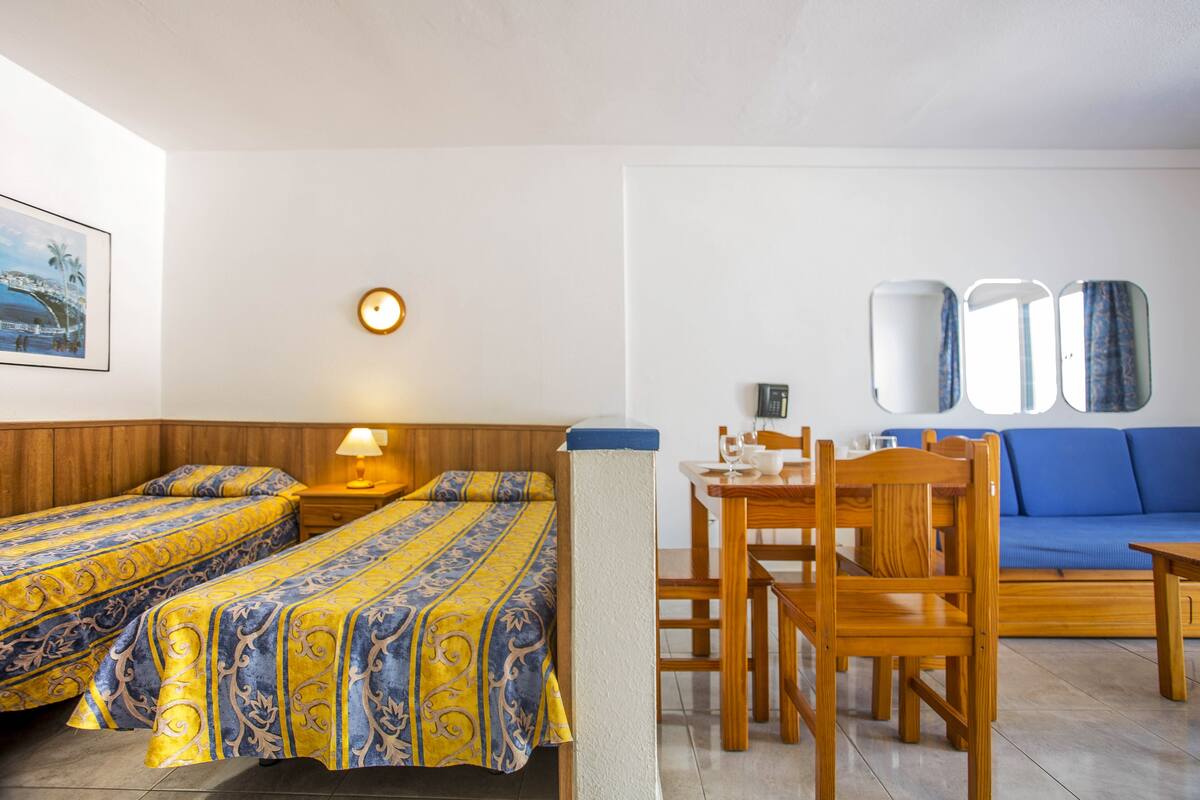 Une chambre d’hôtel avec deux lits, une table à manger avec des chaises, un canapé, une horloge et un miroir fixé au mur.