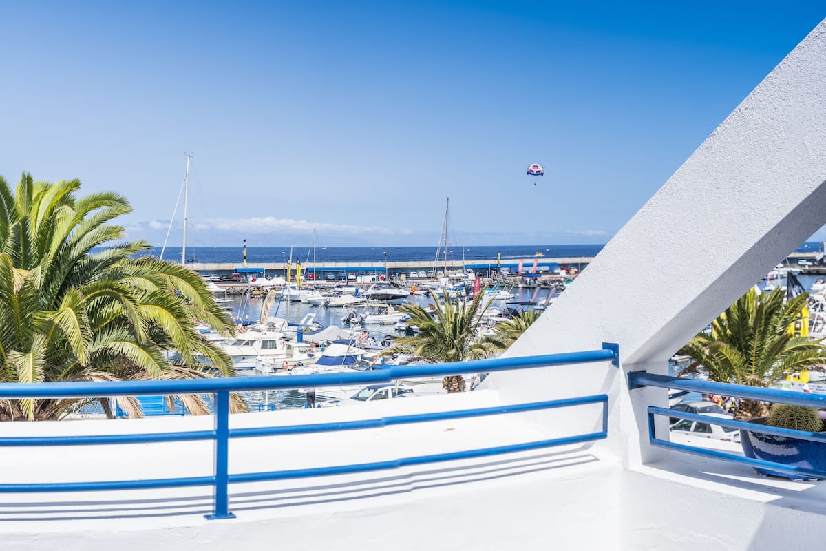 Un port de plaisance où de nombreux bateaux sont amarrés, des palmiers et un ciel bleu azur.