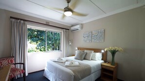 Una habitación de hotel con cama, mesita de noche, escritorio, silla y ventana con cortinas.