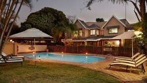 Propiedad residencial con piscina, sillas de descanso y un patio cubierto.