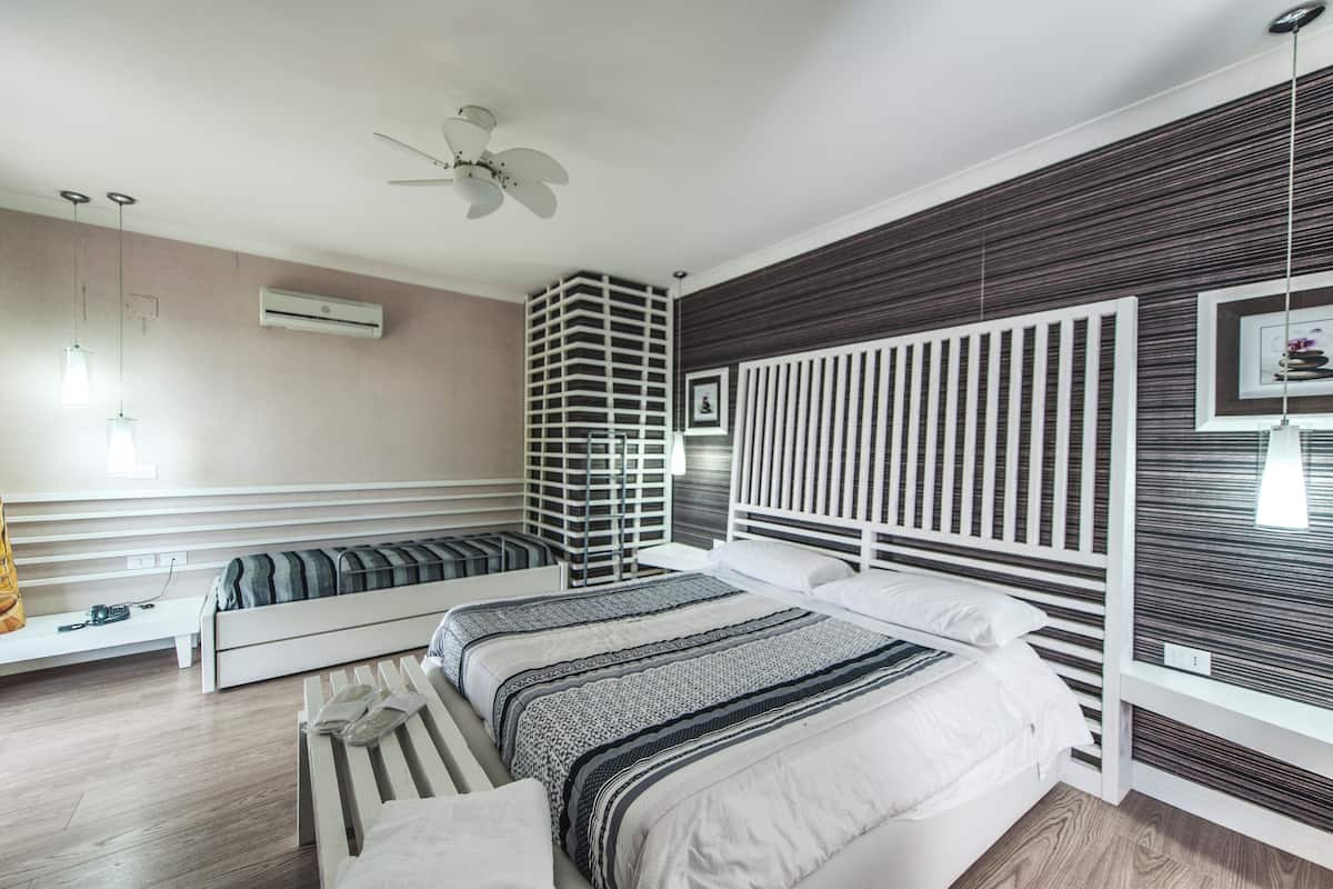 A modern bedroom with a bed, bedside tables, a bench, a ceiling fan, and a wall-mounted air conditioner.