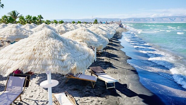 Una spiaggia con ombrelloni di paglia, lettini e una vista libera sull'oceano.