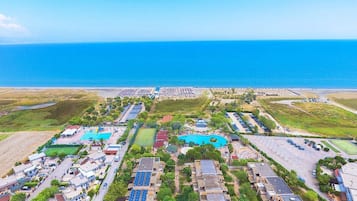Vista aerea di un resort costiero con diverse piscine, pannelli solari e una spiaggia.