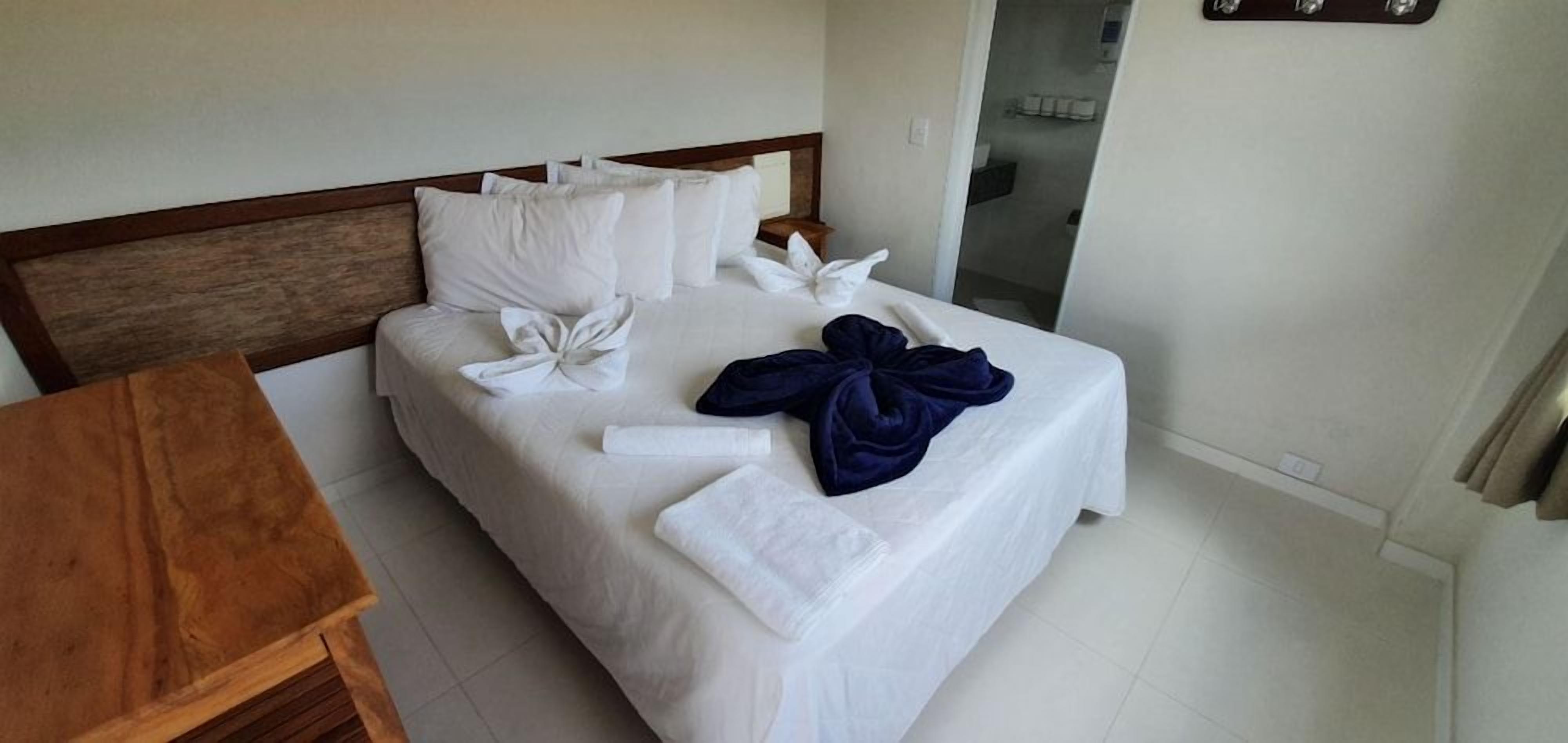 A hotel room with a bed, a wooden nightstand, and a bathroom visible in the background.