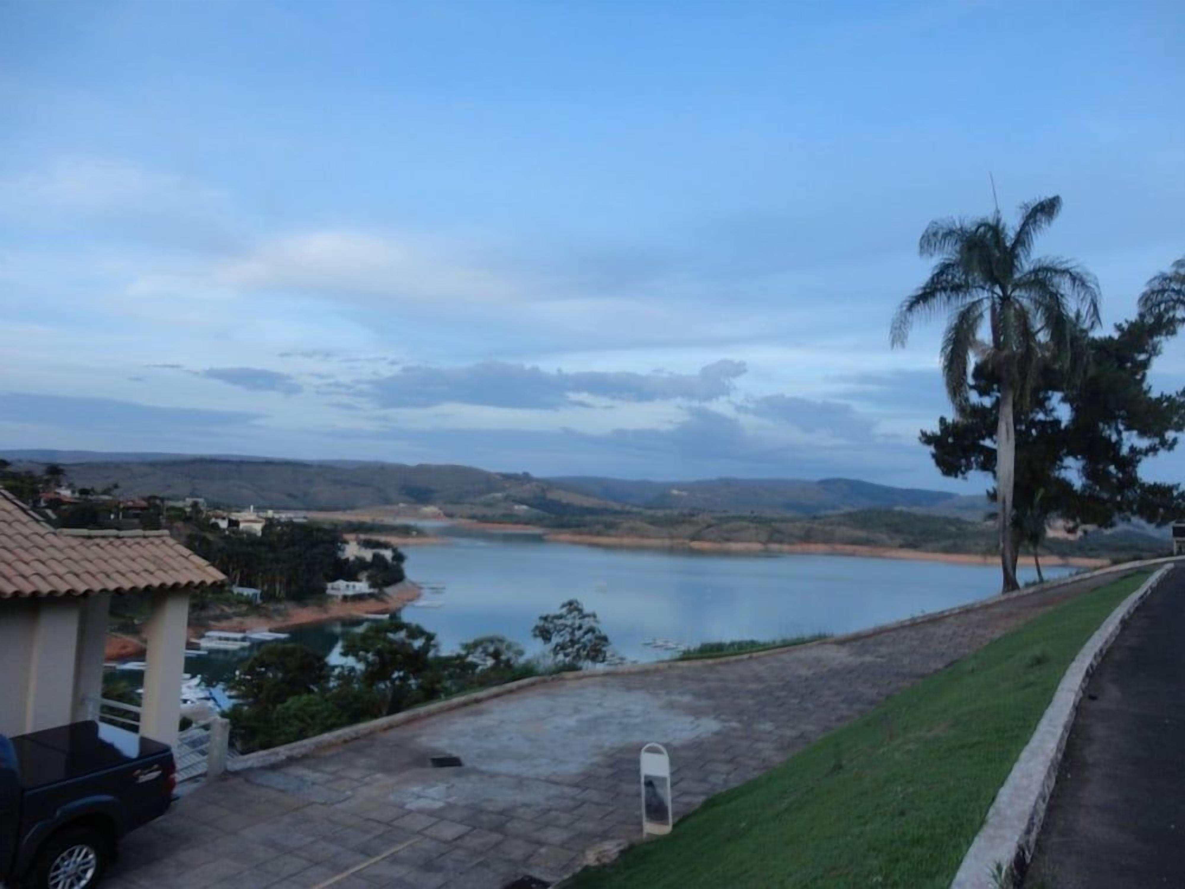 A paved area with a parked vehicle, a palm tree, and a view of a lake with distant hills.