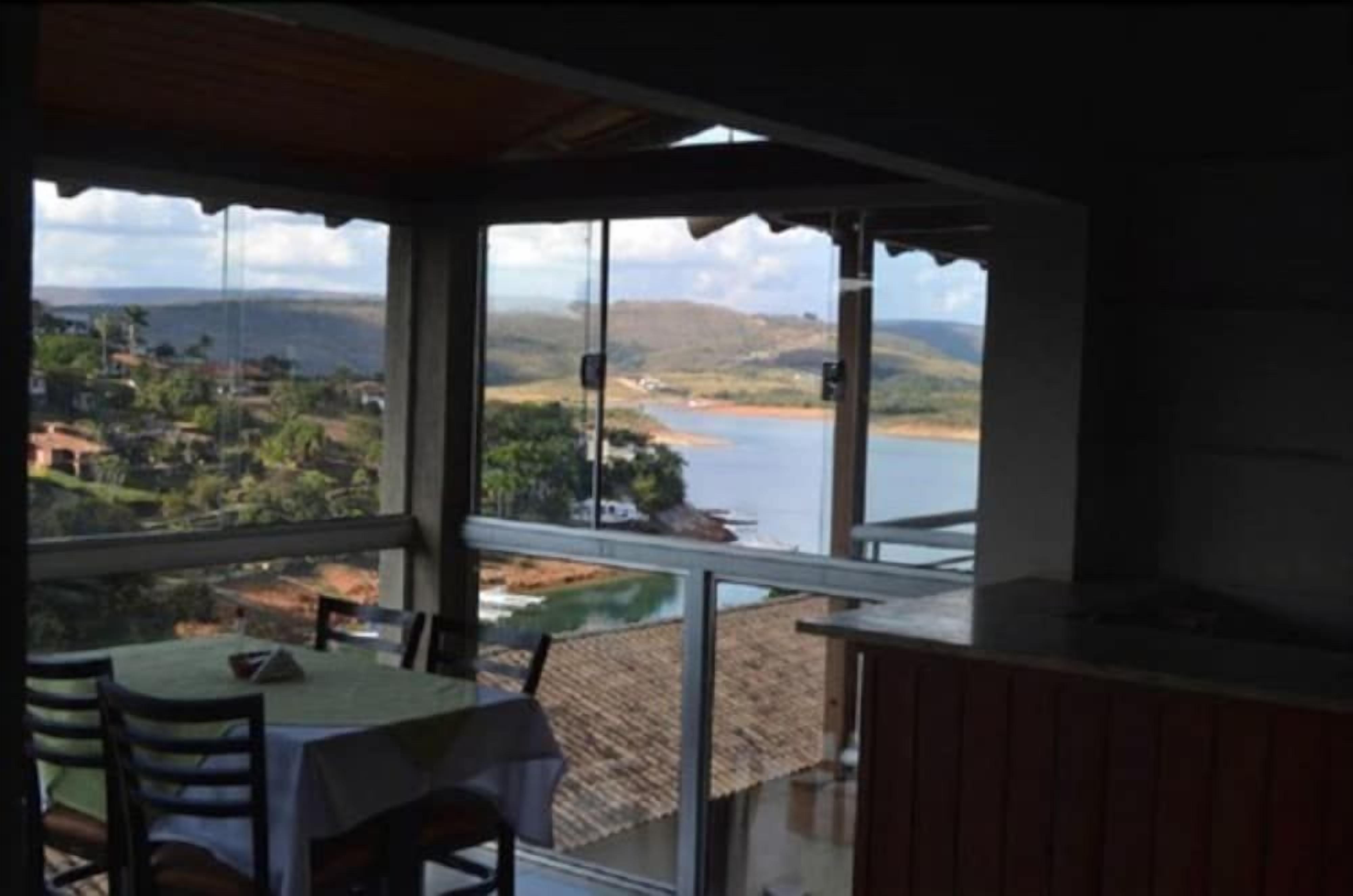 A room with a table and chairs, a view of a lake and hills, and a glass door leading outside.