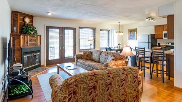 A spacious living room with a fireplace, a sofa, a coffee table, and a kitchen area with a refrigerator, microwave, and dining table. - Crown Resorts at Silverwoods (DuBois)