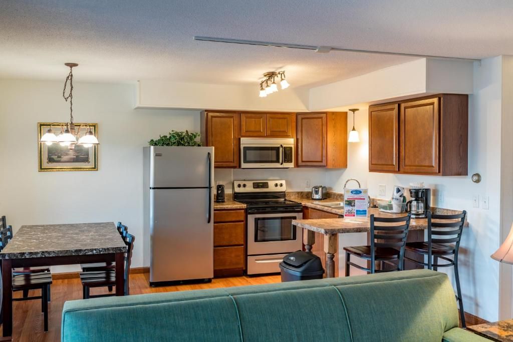 A compact kitchen with wooden cabinets, a refrigerator, a microwave, an oven, and a dining area with a table and chairs.