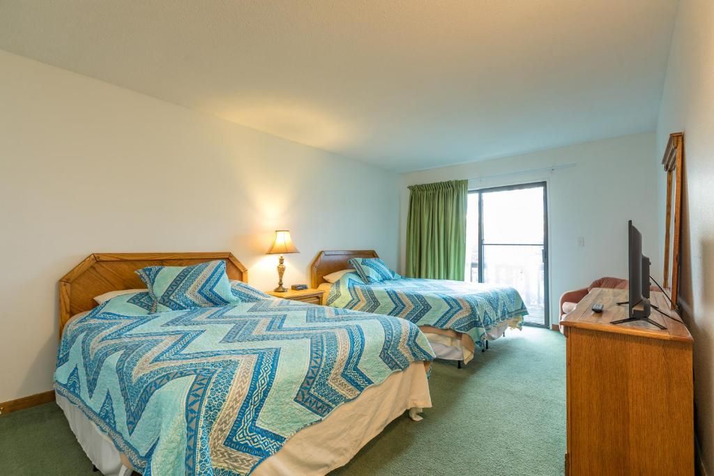Habitación de hotel con dos camas, un escritorio, una lámpara y una ventana con cortinas.