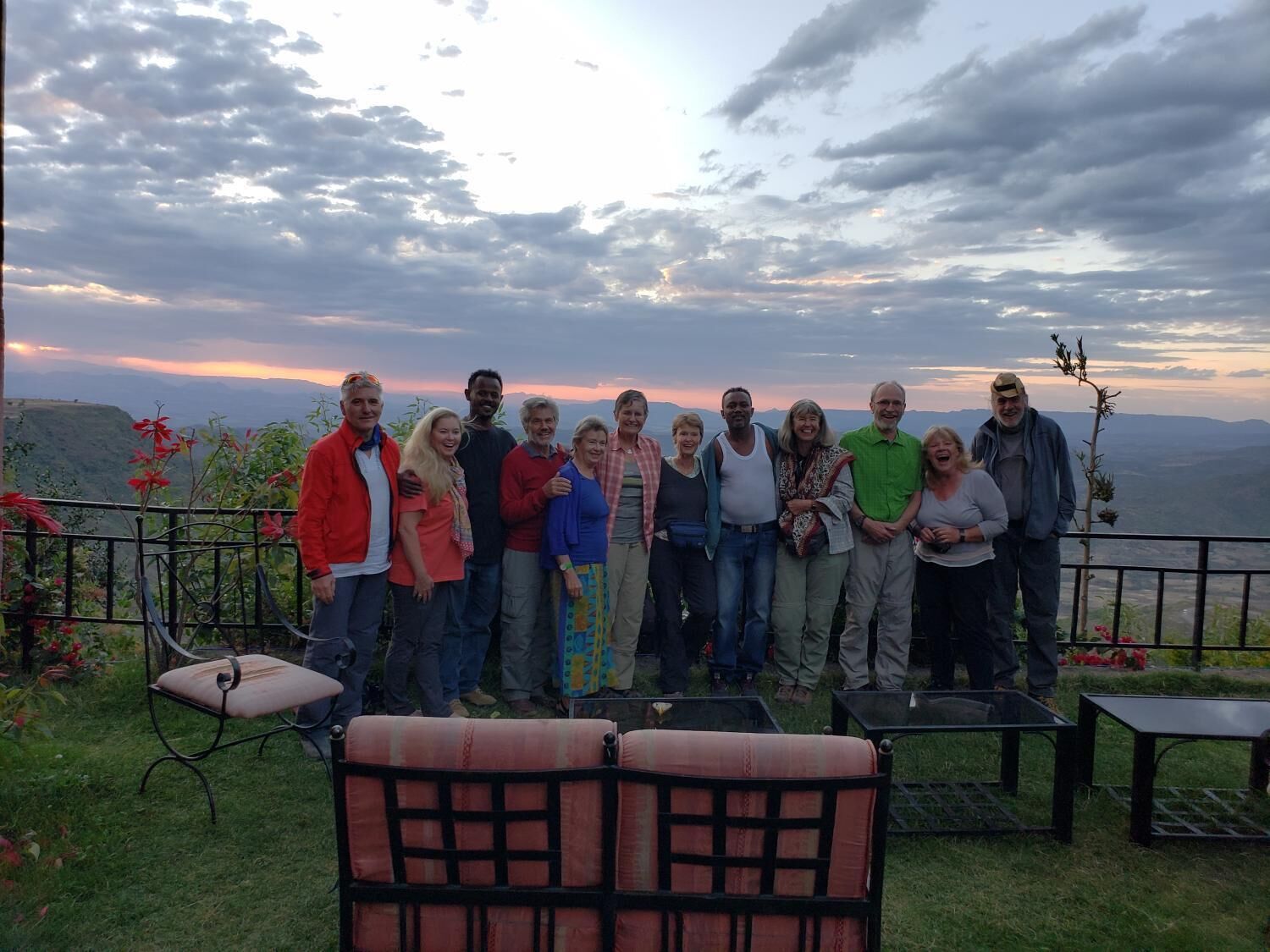 A group of people standing on a balcony with a scenic view of mountains and a sunset.