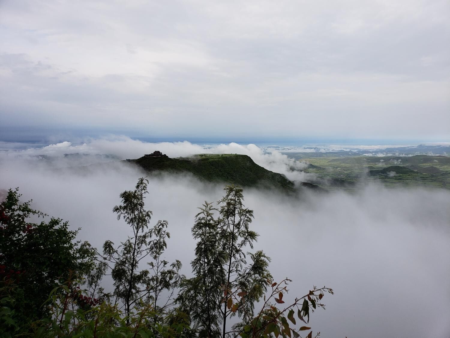 Un paisaje montañoso con una estructura en una colina, rodeada de nubes.