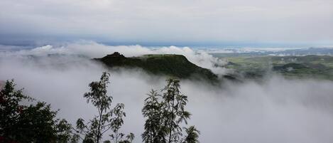 Un paisaje montañoso con una estructura en una colina, rodeada de nubes.