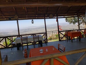 Enjoy al fresco dining with a view of the surrounding hills from this outdoor dining area, featuring comfortable seating and lush greenery.