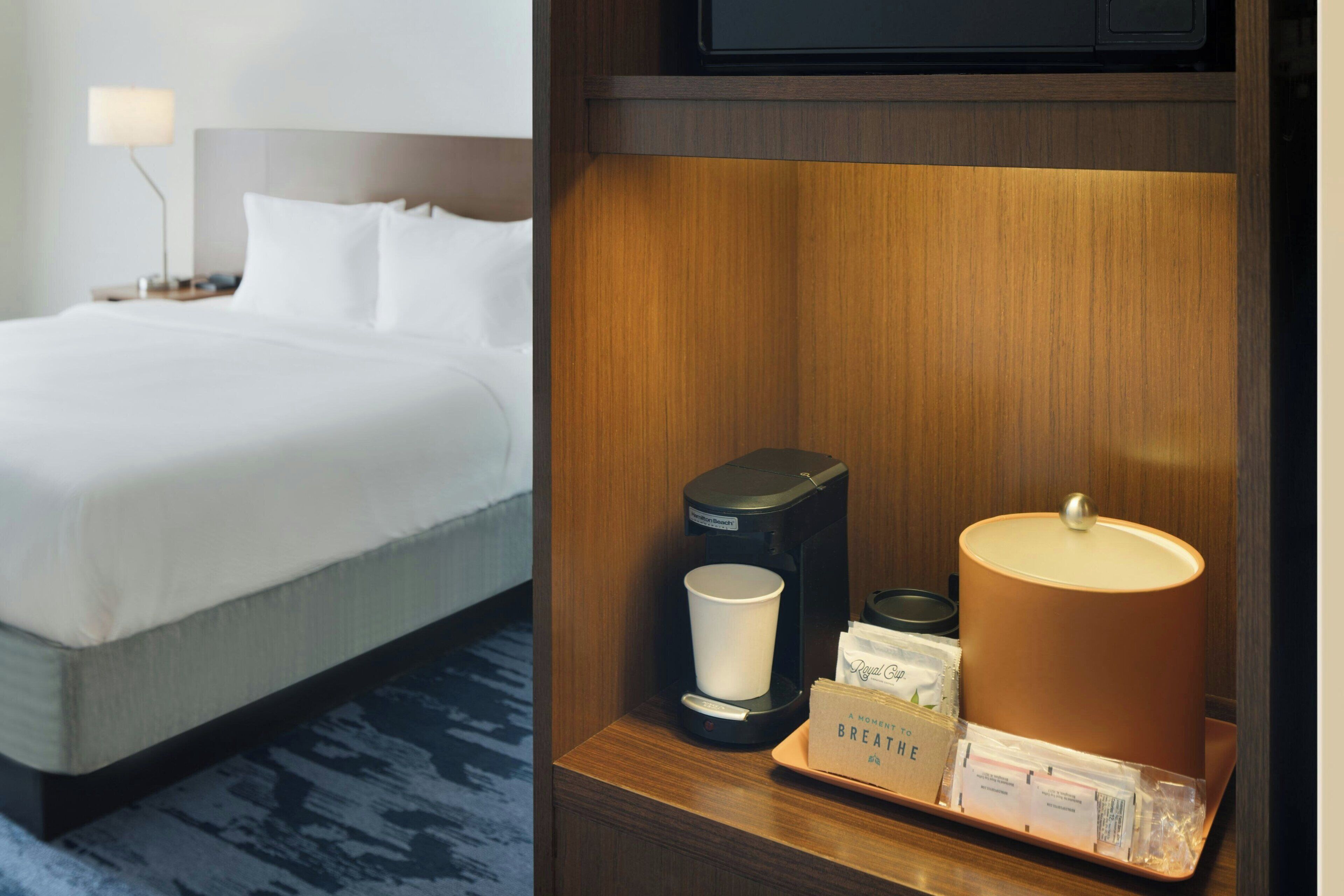 Une chambre d’hôtel avec un lit bien fait, une machine à café, une lampe et un plateau avec des articles de toilette.