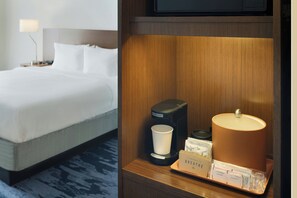 Quarto de hotel com cama arrumada, cafeteira, luminária e bandeja com amenidades.