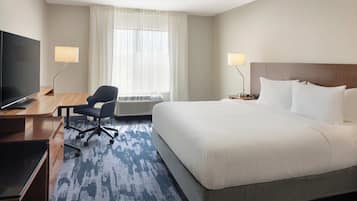 A hotel room with a bed, a desk with a computer, a chair, a TV, and a window with curtains.