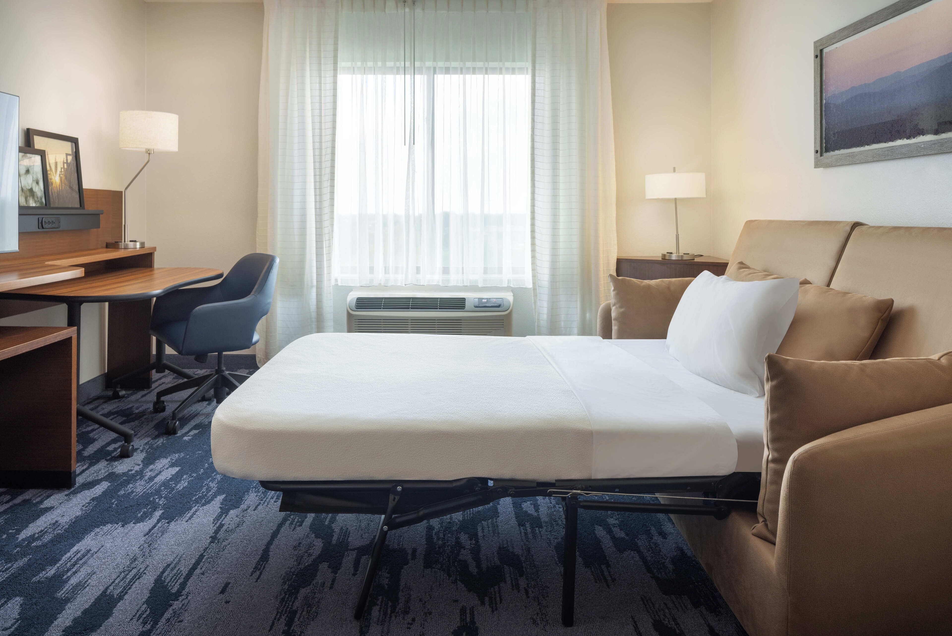 A hotel room with a bed, a desk, a chair, a lamp, and a window with curtains.