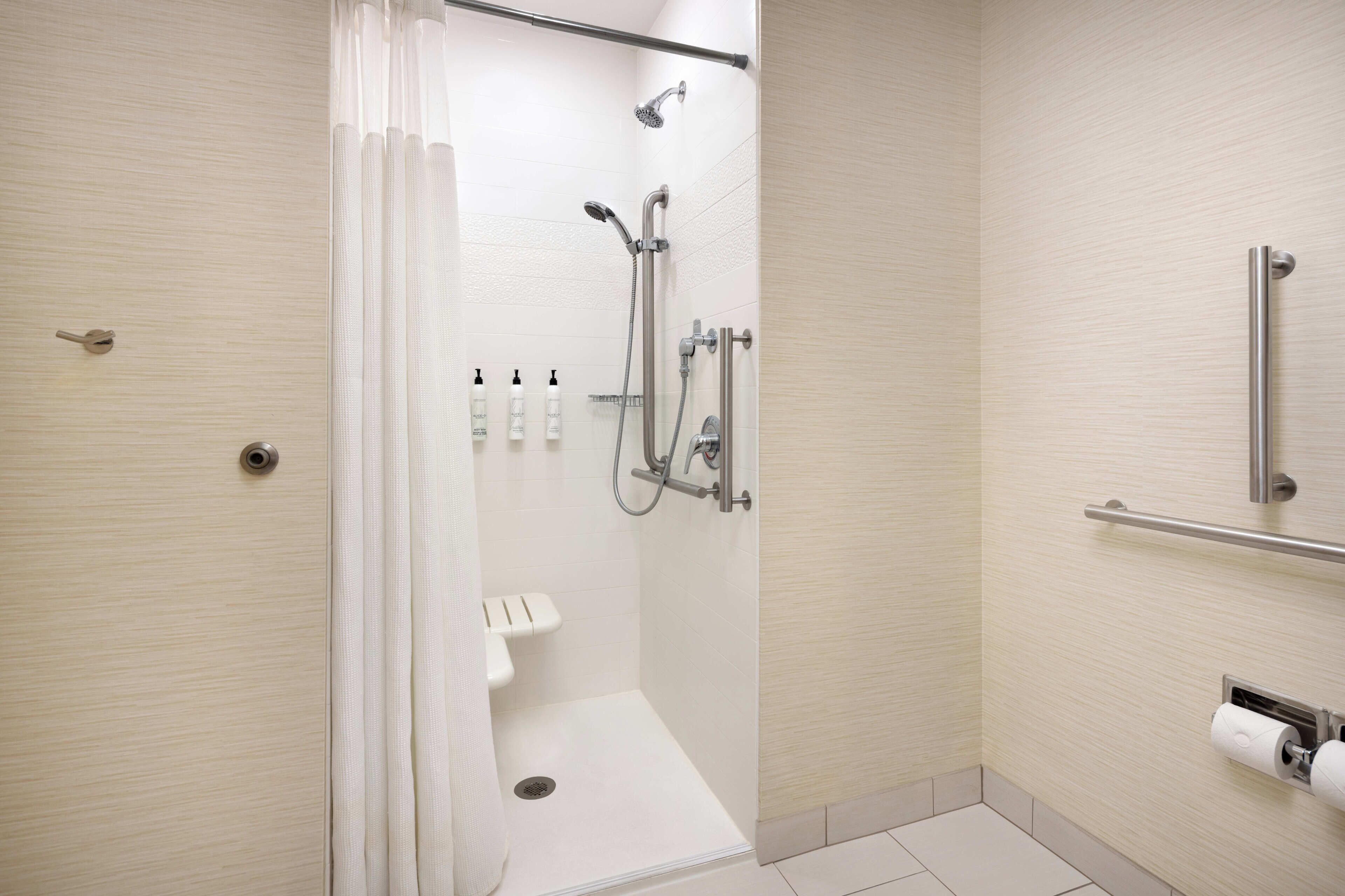 A modern bathroom with a walk-in shower, grab bars, and a toilet paper holder.