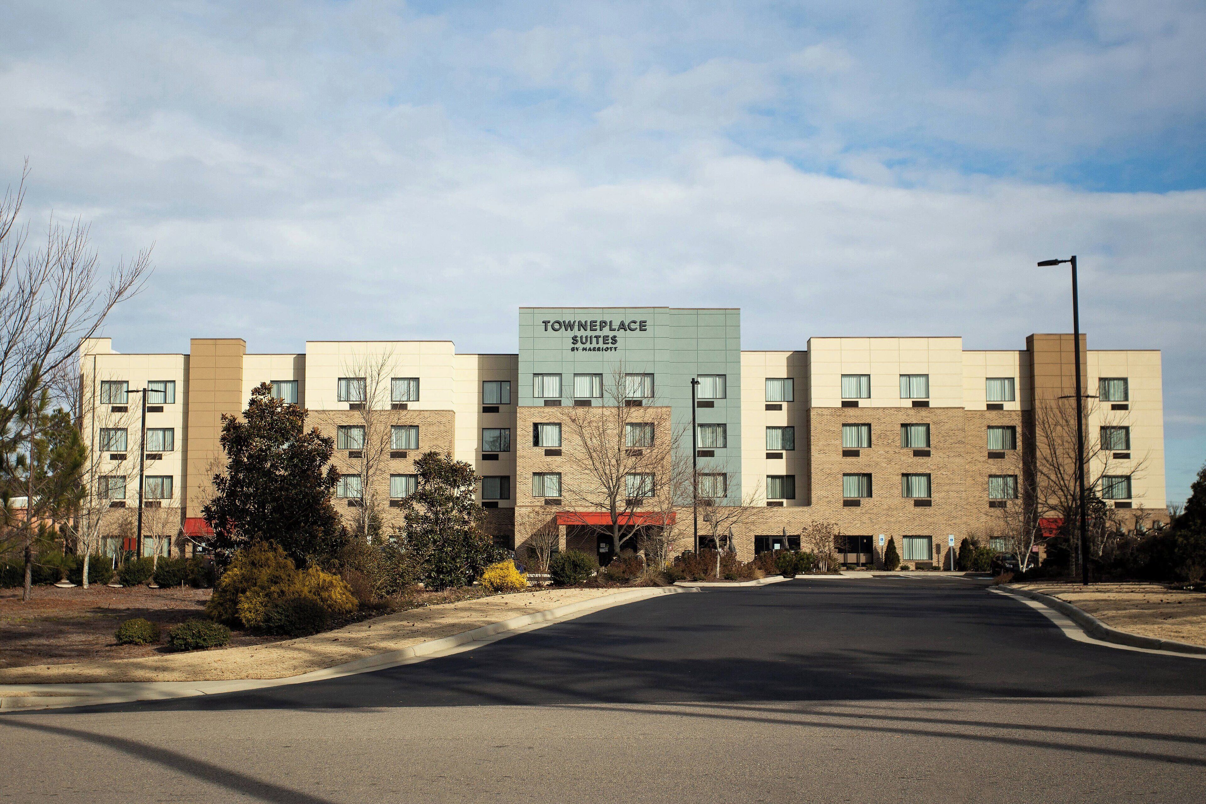 Un hotel de varios pisos llamado TownePlace Suites by Marriott, con un diseño arquitectónico moderno, que cuenta con una entrada central y un estacionamiento al frente.