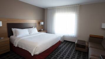 A hotel room with a large bed, a nightstand, a lamp, a sofa, and a window with curtains.
