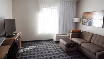 Une chambre d’hôtel avec un canapé, un bureau équipé d’un ordinateur, une lampe et une fenêtre avec des rideaux.