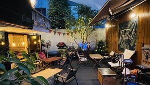 An outdoor patio area with wooden tables and chairs, a small Christmas tree, and a tiki bar. - Bunk Guest House - Hostel (Seoul)
