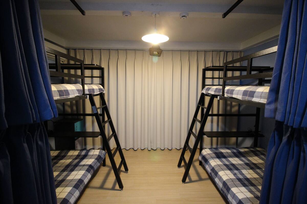 Une chambre avec des lits superposés, un luminaire au plafond et un rideau.
