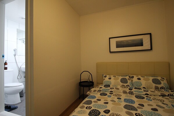 A bedroom with a bed, a framed picture on the wall, and a small table with a candle.