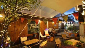 An outdoor seating area with wooden tables and chairs, string lights, and potted plants. - Bunk Guest House - Hostel (Seoul)