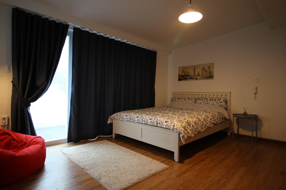 Une chambre à coucher avec un lit, un fauteuil en forme de sac de haricots rouge, une petite table et un tableau accroché au mur.