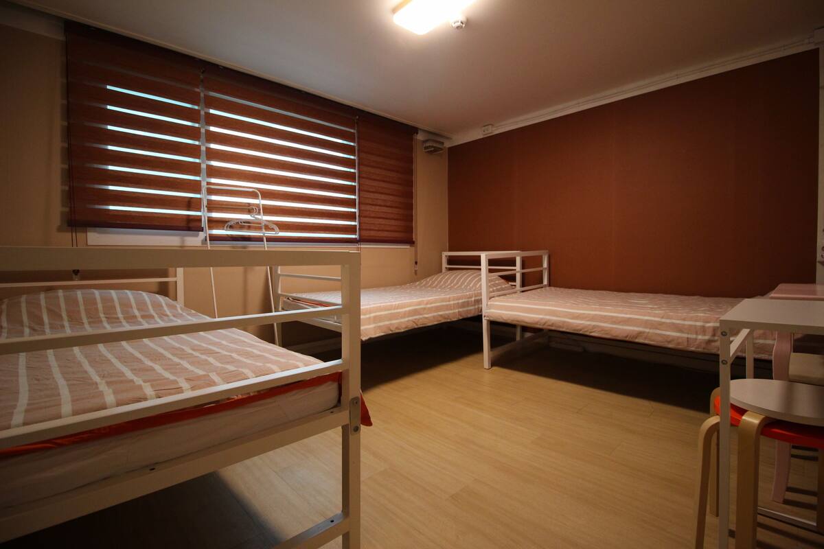 Une chambre de dortoir avec des lits superposés, une fenêtre avec des stores, un bureau et une chaise.