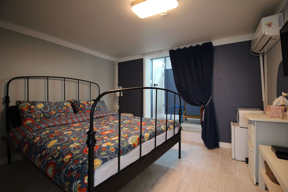 Une chambre à coucher comprenant un lit, un bureau, une chaise, une fenêtre avec des rideaux et un climatiseur.