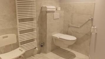 A modern bathroom with a shower, toilet, and a white chair.