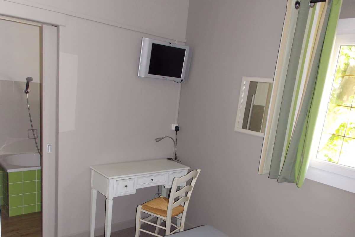 Quarto com uma cama de solteiro, uma escrivaninha com cadeira, televisão fixada na parede e janela com cortinas.