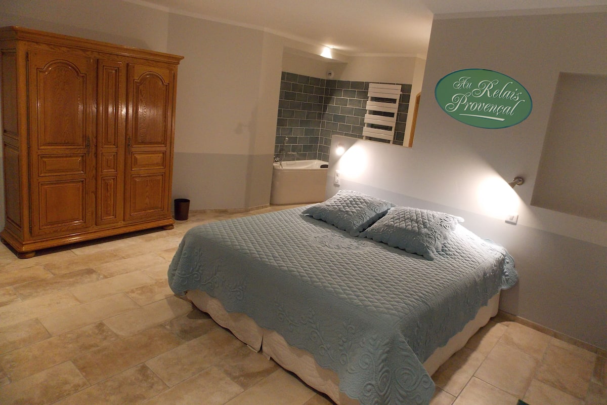 Quarto com um guarda-roupa de madeira grande, cama com colcha acolchoada e luminária fixada na parede.